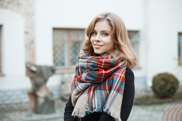 Street female portrait of a beautiful young woman with a fashion vintage plaid scarf in a black coat in the city