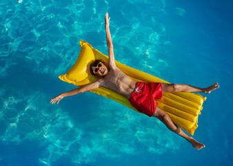 Relaxed swimmer afloat in pool on a yellow raft view from above - obrazy, fototapety, plakaty