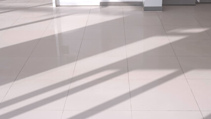 Sunlight and long shadow pattern of glass wall frame on surface of gray ceramic tile floor inside of living room, high angle view with copy space
