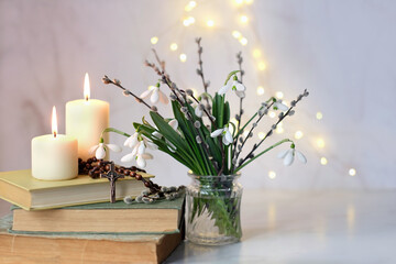 Bouquet of snowdrop flowers, christian rosary beads, religion books and candles on table, abstract...