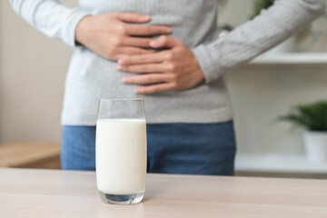 Fototapeta na wymiar Pain, suffering asian young woman having a stomachache, abdominal pain or digestive, hand in holding belly after drink glass of milk. Lactose intolerance, allergy from dairy food, health care problem.