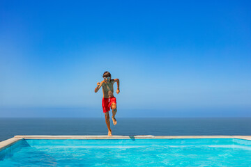 Cute teen leap playfully into a swimming pool against sea view