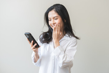 Fototapeta premium Happy asian young woman using mobile smart phone, read good news online feel excited getting offer, great positive surprise, celebrate success on smartphone. Businesswoman isolated on white background