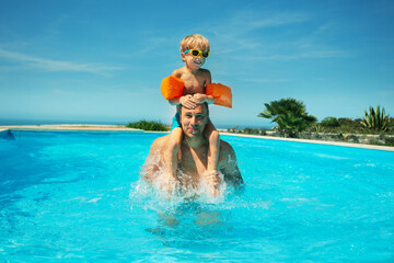 Child rides shoulders of dad in sunny swimming pool outside