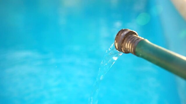 Close up stream of water flowing from a green hose and filling a clean blue swimming pool in the backyard. Weekly pool maintenance and cleaning