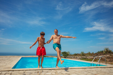 Father and son enjoy pool jump backwards together in summer