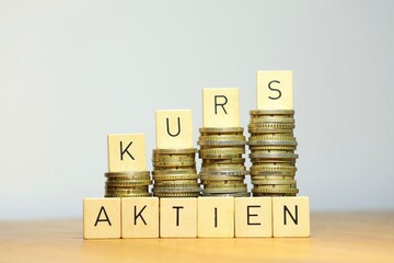 Finanzieller Erfolg durch Aktien und aktuelle Entwicklung auf dem Aktienmarkt symbolisiert durch Geldstapel vor hellem, neutralem Hintergrund, Copyspace und den Schriftzug Aktienkurs