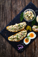 Tasty sandwich with egg salad and smoked mackerel on wooden table
