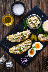Tasty sandwich with egg salad and smoked mackerel on wooden table
