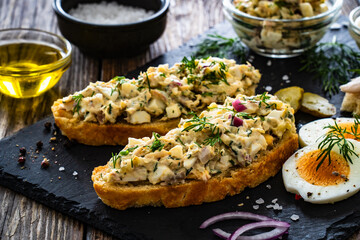 Tasty sandwich with egg salad and smoked mackerel on wooden table
