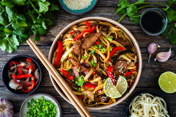 Asian style stir fried vegetables, roast beef and chow mein noodles  to go  in food box on wooden table
