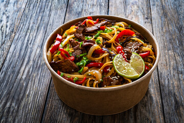 Asian style stir fried vegetables, roast beef and chow mein noodles  to go  in food box on wooden...
