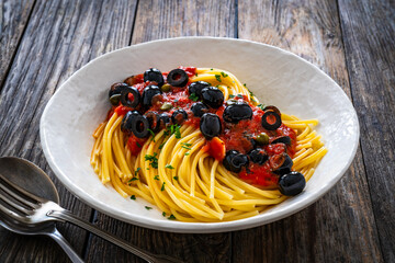 Spaghetti puttanesca with tomato sauce, anchovies, chili, capers and black olives on wooden table
