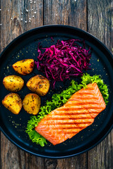 Grilled salmon steak with baked potatoes and  red cabbage  on black plate on wooden table
