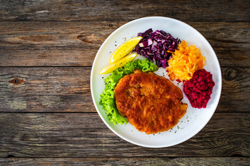 Crispy breaded fried pork chop with grated beetroots, red cabbage and sauerkraut on wooden table
