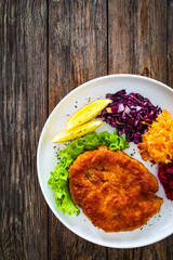 Crispy breaded fried pork chop with grated beetroots, red cabbage and sauerkraut on wooden table
