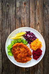 Crispy breaded fried pork chop with grated beetroots, red cabbage and sauerkraut on wooden table
