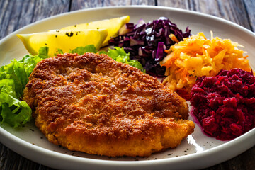 Crispy breaded fried pork chop with grated beetroots, red cabbage and sauerkraut on wooden table
