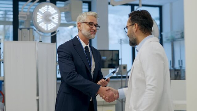 Pharmaceutical sales representative presenting new medication to doctor in medical building, shaking hands.