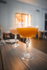Two elegant glasses with orange cocktails on a dark wooden table, sharply focused in a blurred modern interior with warm lighting, suggesting a serene spa resort ambiance.