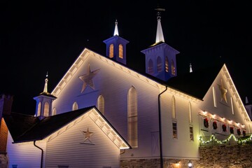 Illuminated White Church Adorned With Christmas Wreaths And Stars At Night, Showcasing Its...