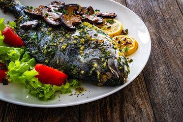 Baked sea bream, mushrooms and fresh vegetables on wooden table
