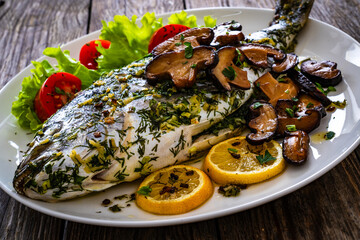 Baked sea bream, mushrooms and fresh vegetables on wooden table

