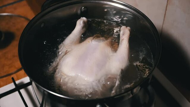 Cooking a Whole Chicken Carcass in a Pot of Boiling Water in a Home Kitchen. Close up. Rich chicken broth, broiler chicken leg soup. Smoke, steam. Homemade lunch or dinner. Poultry meat dishes. Food.