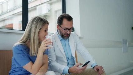 Doctor and nurse taking a break during work shift at hospital, drinking water and talking.