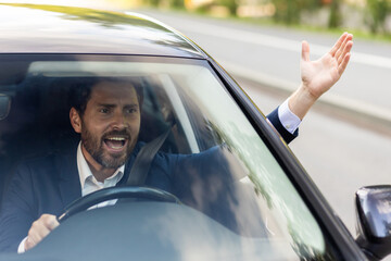 Close-up photo of an angry young businessman driving a car, shouting and waving his hands