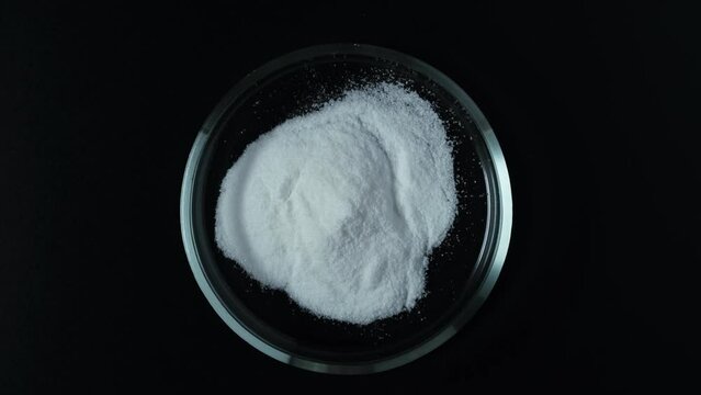 Sodium erythorbate or isoascorbate in Petri dish. Food additive E316, chemical formula C6H7NaO6. Chemically, it is the sodium salt of erythorbic acid. White crystalline powder. 4K video, rotating.