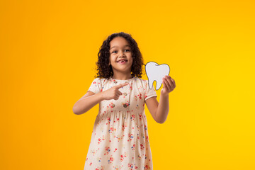 Child girl holding papercraft tooth and pointing finger at it. Dental health concept