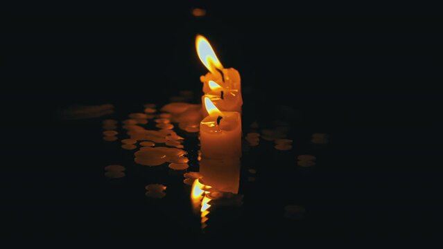 Three paraffin candles burn in a row on a black background with reflection. Three white candles burn with a bright orange flame on a dark background. Symbol of sadness, memory of the dead, war concept