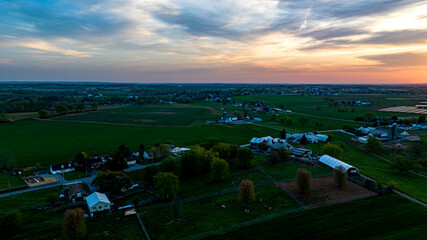 Sunset Casts A Warm Glow Over A Rural Farmland Tapestry With Homes, Barns, And Lush Fields Under A Dynamic Sky. © Greg Kelton