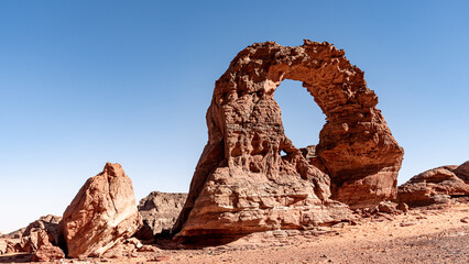 Tadrart landscape in the Sahara desert, Algeria. A delicate red sandstone arch has been sculpted by the wind and sand of the Tadrart - 732660836