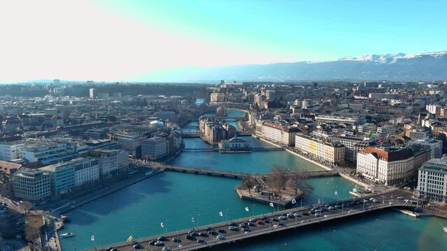 Flight over sunny Geneva central cityscape lakeside rooftop aerial panorama ft. Bel-Air Bridge around Rhone River, Lake Geneva. Swiss Alps in the background 4K