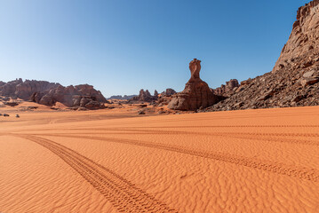 Landscape of the Red Tadrart in the Sahara Desert, Algeria. Tire tracks in the sand in front of a sandstone peak reminiscent of the football World Cup trophy