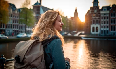 Deurstickers Evening Elegance in Amsterdam: A 45-50-Year-Old Happy Tourist Woman, Backpack On, Enjoying a Canal Cruise with Historic Buildings Illuminated at Dusk.      © Mr. Bolota