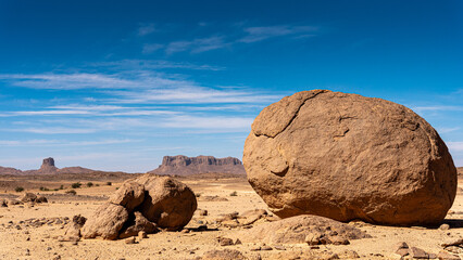 Hoggar landscape in the Sahara desert, Algeria. A large round stone with a wild west decor in the background - 732663425