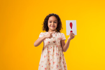 Smiling kid girl holding exclamation point card and pointing finger at it. Children, idea and...