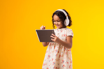Smiling kid girl with headphones using tablet. Lifestyle, leasure and gadget addiction concept