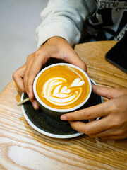 Female hands holding cup of hot latte art coffee on wooden background