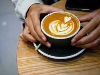 Female hands holding cup of hot latte art coffee on wooden background