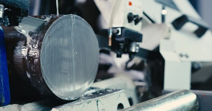 The automatic band saw machine cutting the metal rod. The machine tool operation with liquid coolant.