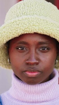 Vertical individual close up portrait of beautiful African American young adult woman looking at camera with serious expression standing outdoors. High quality footage
