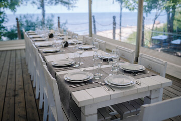 Jurmala, Latvia - july 25, 2023 - Elegant outdoor dining setup on deck with a long table set with plates, glasses, and silverware, overlooking the sea.