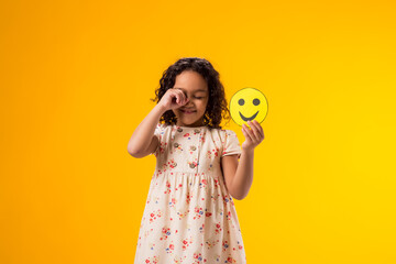 Crying kid girl holding happy emoticons. Mental health, psychology and children's emotions concept