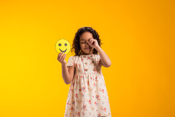 Crying kid girl holding happy emoticons. Mental health, psychology and children's emotions concept