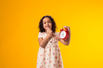 Thoughtful kid girl holding an alarm clock in hand. The concept of education, school, deadlines,...