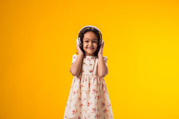 Smiling kid girl enjoying music in headphones on yellow background. Lifestyle and leasure concept